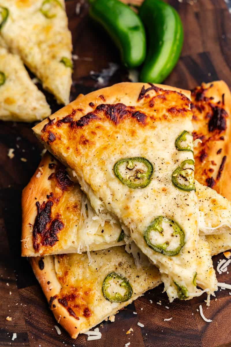 Slices of jalapeño scalloped potato pizza are stacked on top of each other with whole jalapeños in the background.