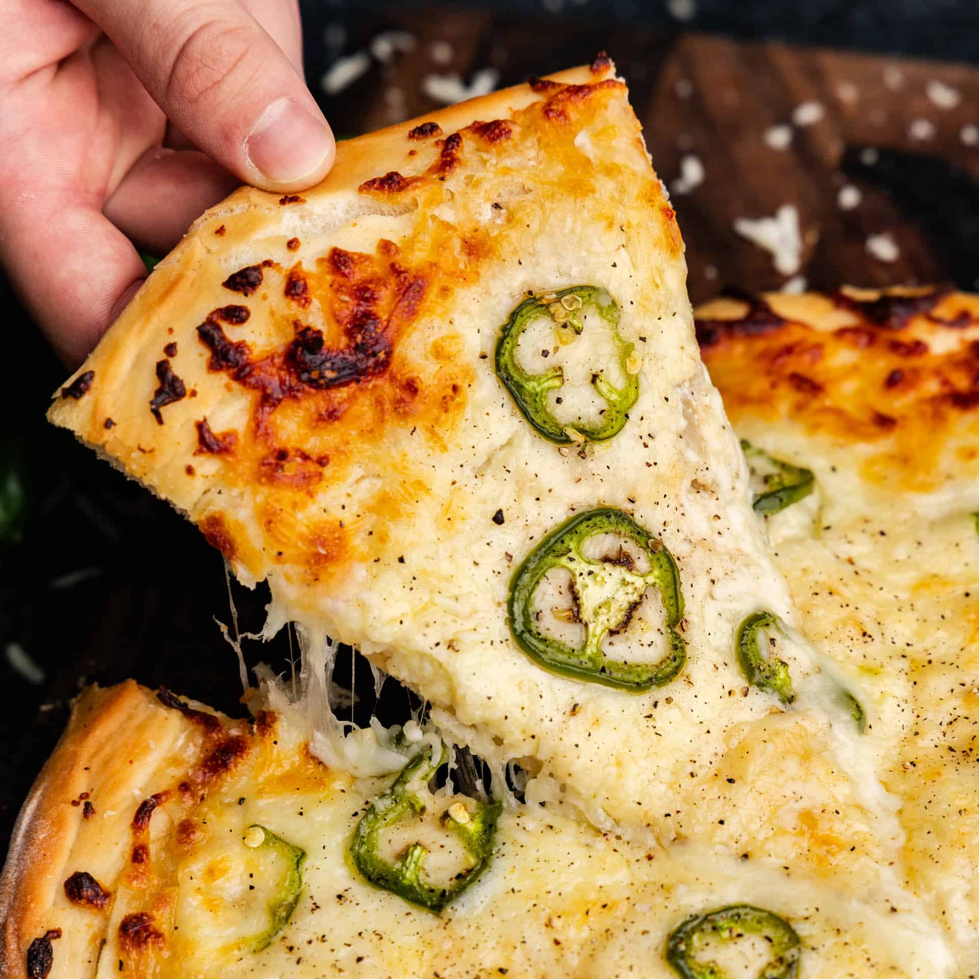 A hand pulling a slice of Jalapeno Scalloped Potato Pizza from the whole pie, with melty cheese stretching.