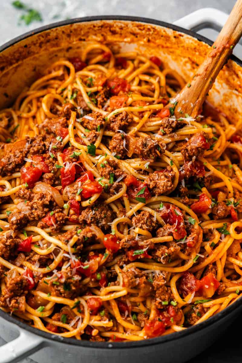 A close-up of cooked spaghetti noodles mixed with red tomato sauce and ground beef, a wooden spoon placed in the corner.