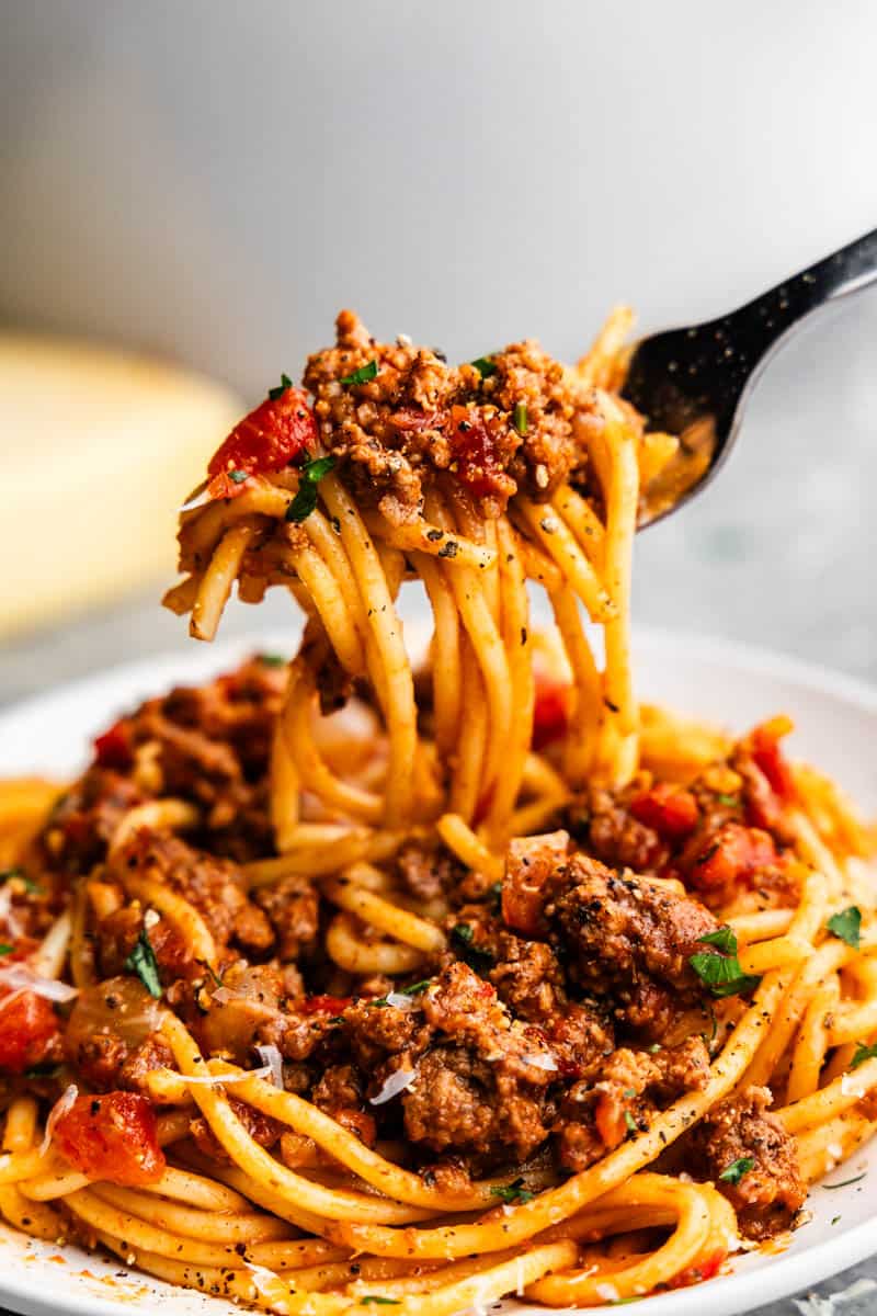 A close up of a bite of spaghetti noodles with meaty sauce taken from a plate.