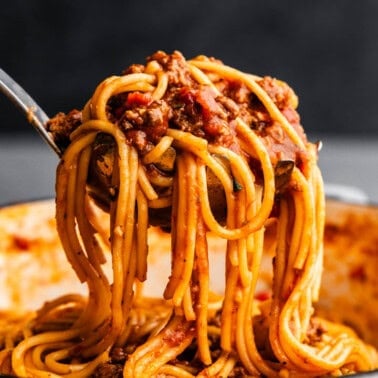 A large serving of saucy spaghetti being lifted from a pot.