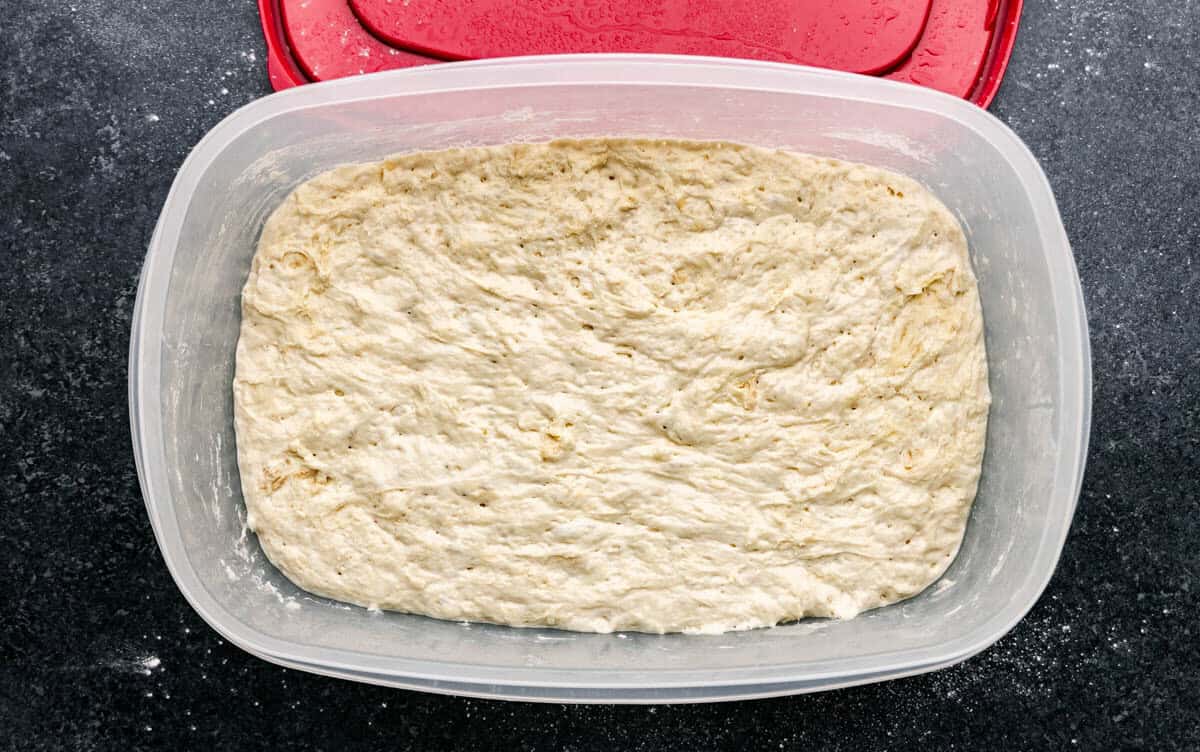 An overhead view of a large container full of refrigerator pizza dough.