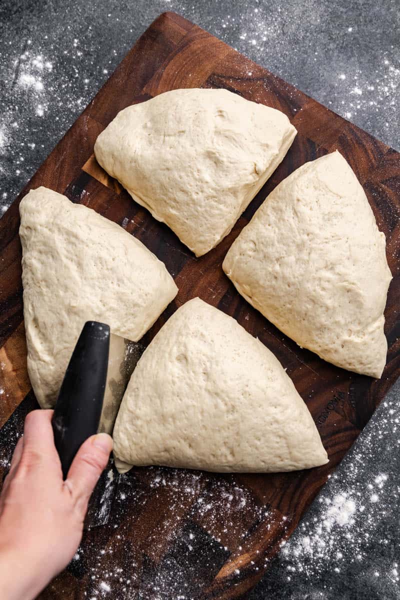 An overhead view of 4 pieces of dough on a wooden cutting board.