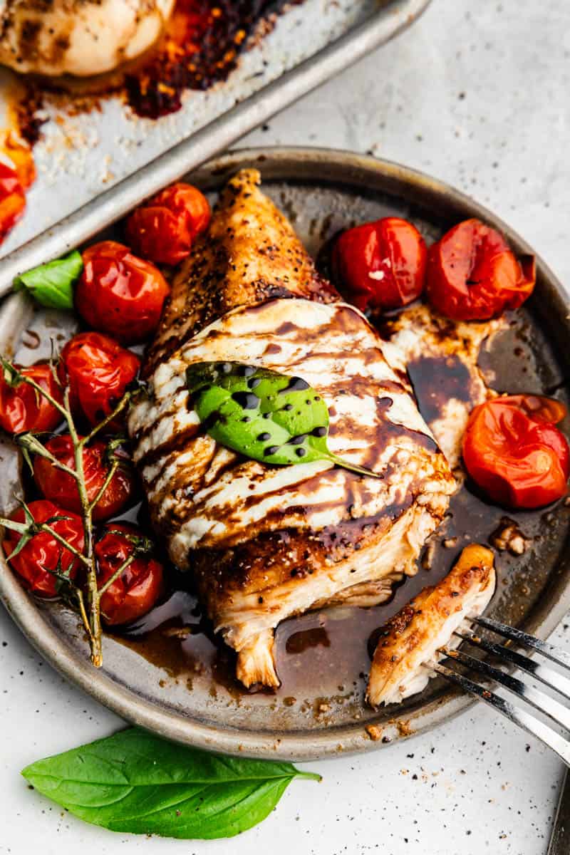 An overhead view of a plate of chicken caprese with roasted tomatoes.