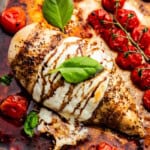 A close up view of a caprese chicken breast surrounded by roasted tomatoes.