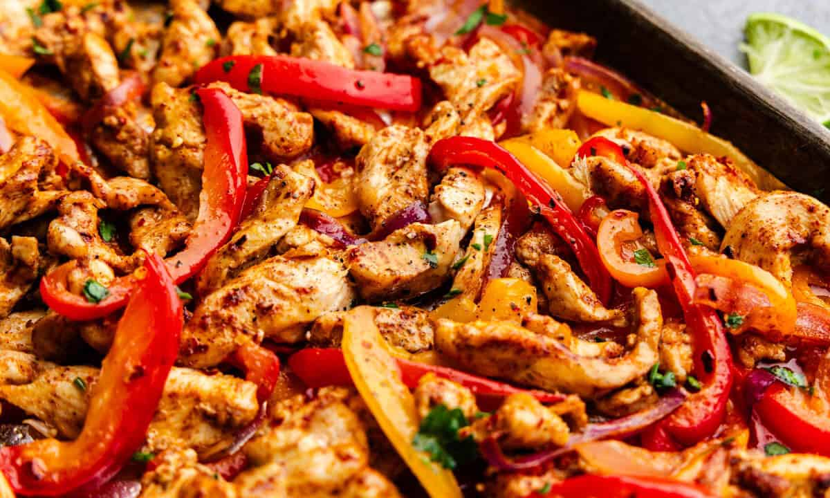 A close up view of a sheet pan filled with cooked chicken fajitas.