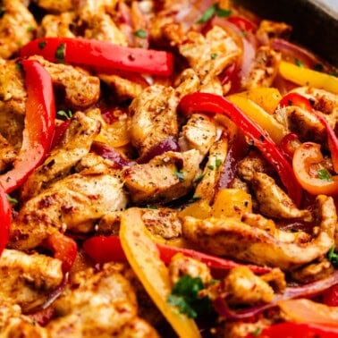 A close up view of a sheet pan filled with cooked chicken fajitas.