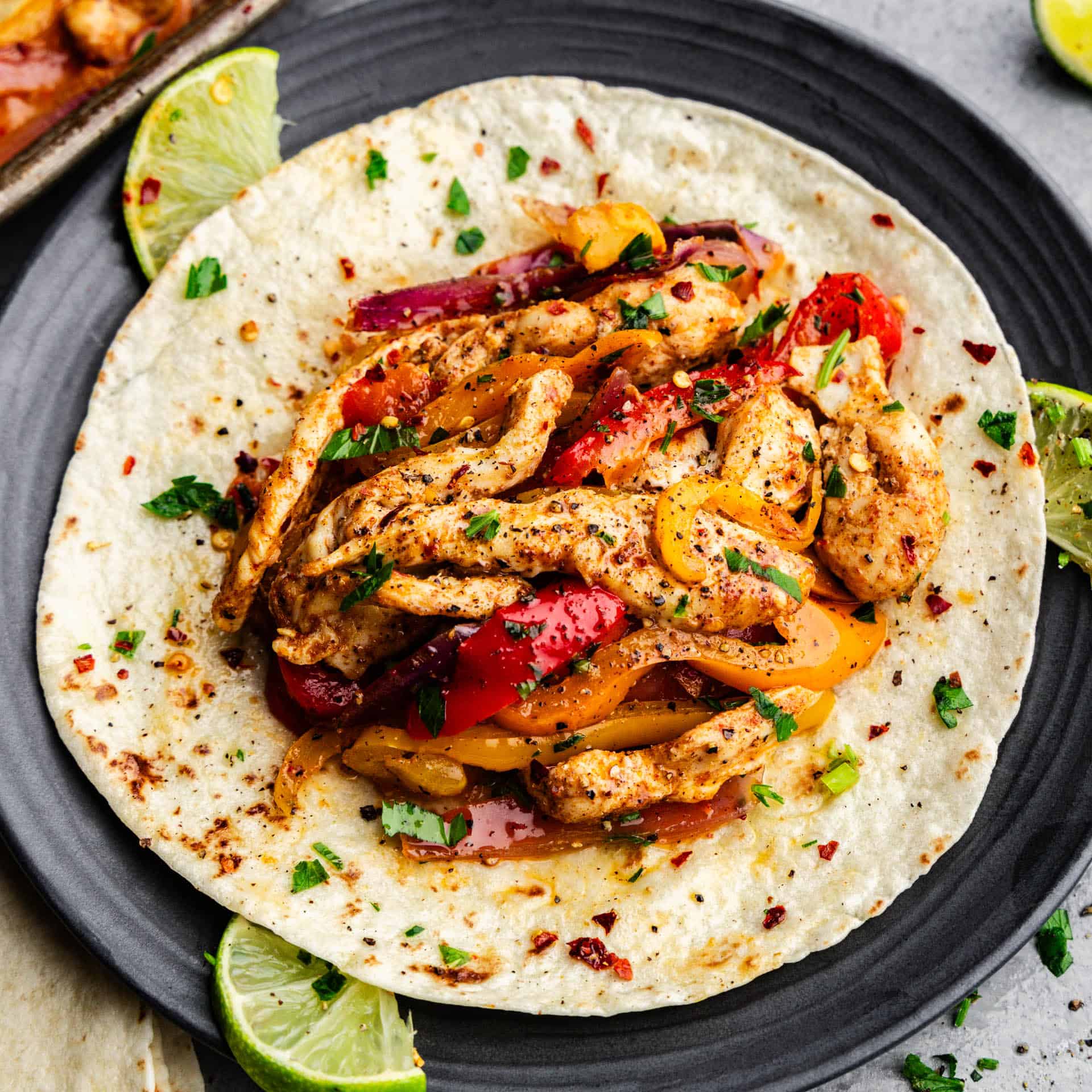 A plate topped with a flour tortilla topped with chicken fajitas, set next to lime slices.