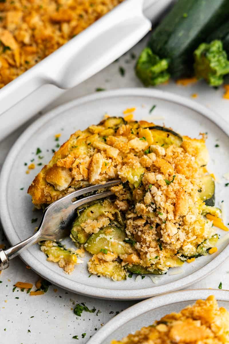 A portion of zucchini casserole on a plate with a fork getting ready to take a bite.