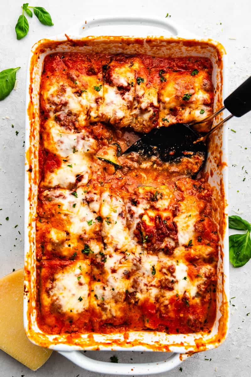 An overhead view of a casserole dish filled with saucy, cheesy zucchini lasagna with a square portion removed.