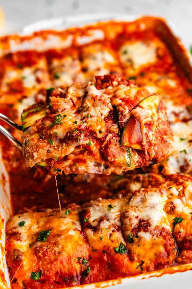 A close-up of zucchini lasagna squares being lifted from the casserole pan.