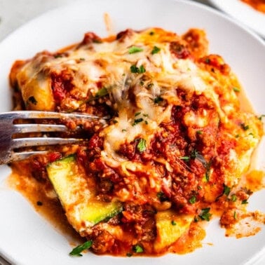 A plate with a serving of zucchini lasagna and a fork set on the plate.