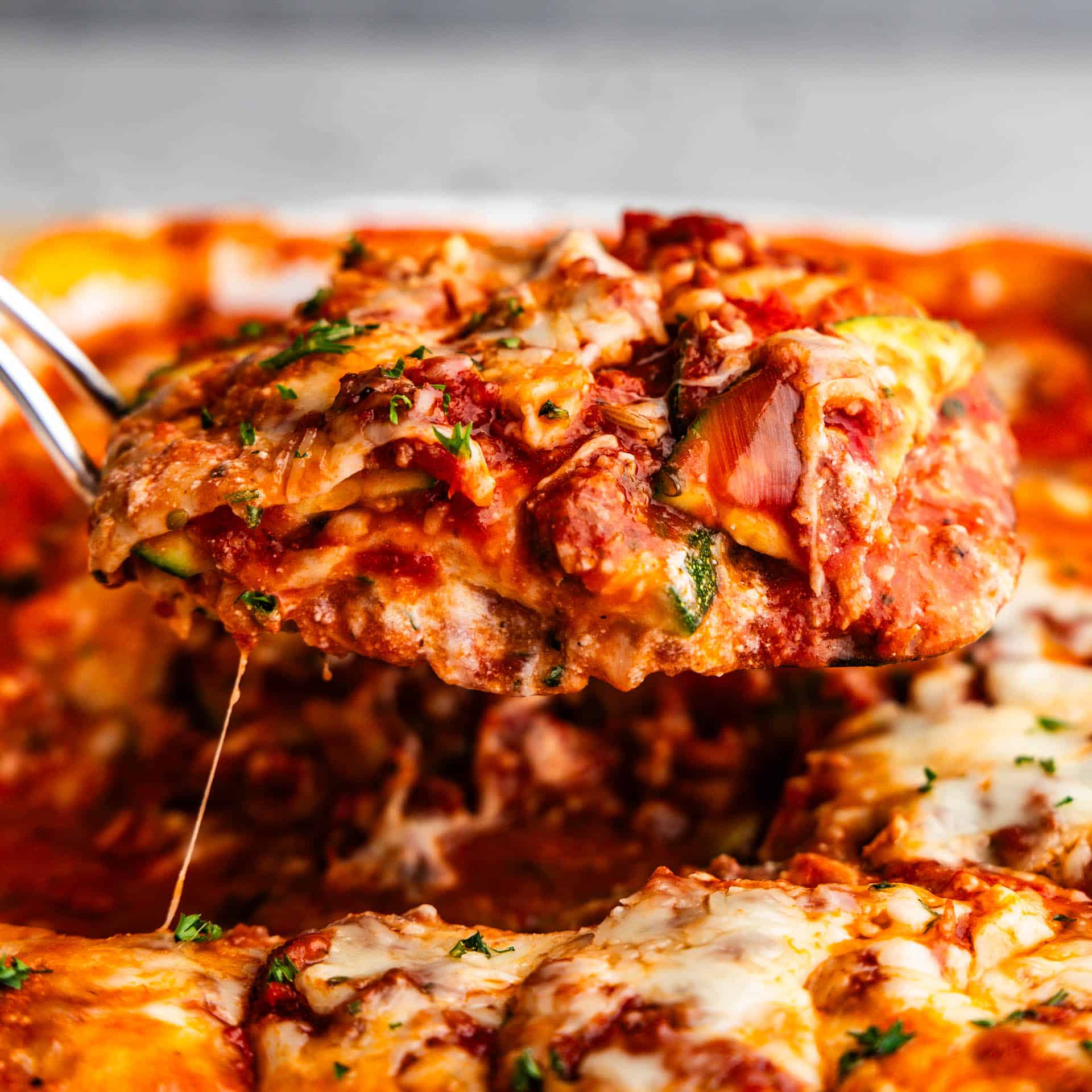 A close up side view of a square of zucchini lasagna being lifted from the casserole dish.