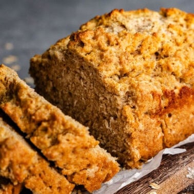 A loaf of beer bread sitting on a wooden cutting board. Two slices have already been cut out.