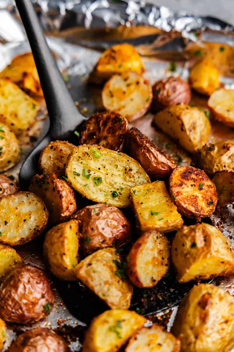 A close up of a spatula sliding under cooked and seasoned pieces of breakfast potatoes.