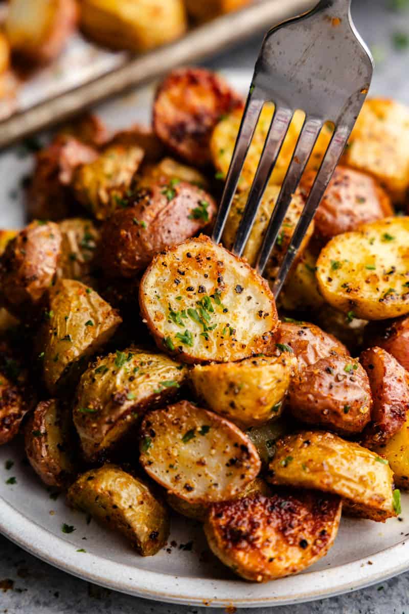 A fork piercing into a golden seasoned piece of potato on a plate loaded with breakfast potatoes.