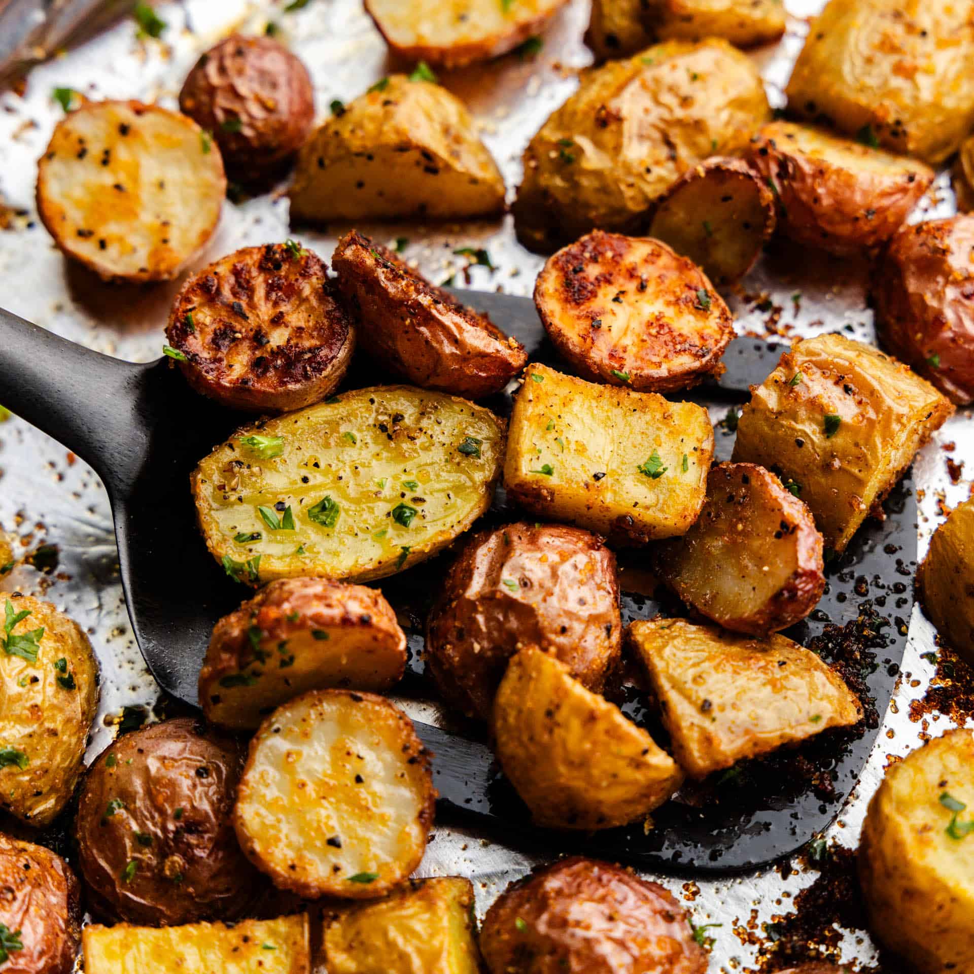 An overhead close up of a spatula filled with breakfast potatoes getting ready to serve them from the sheet pan.