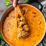 An overhead view of a pot of Cajun white chicken chili with a spoon dishing out a serving.