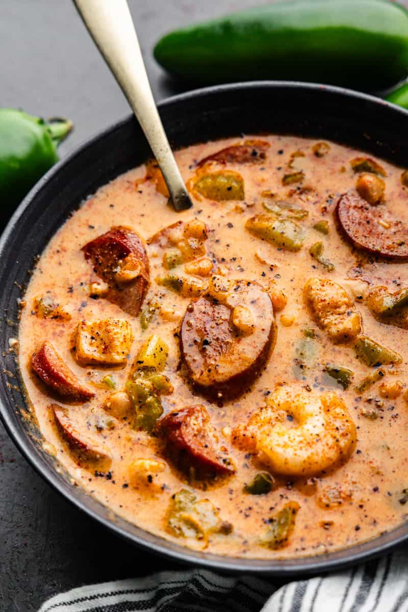 A close-up view of a black bowl of Cajun white chicken chili with shrimp and andouille sausage.