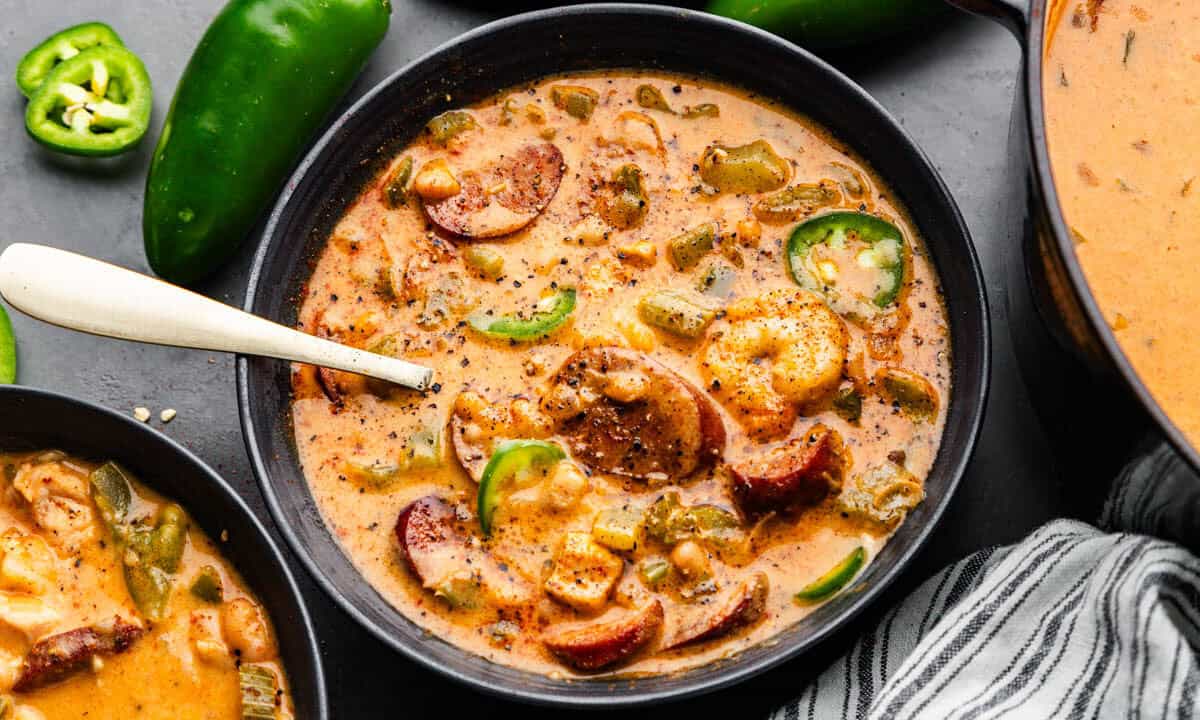 An overhead view of a black bowl of Cajun white chicken chili with a spoon sticking out.