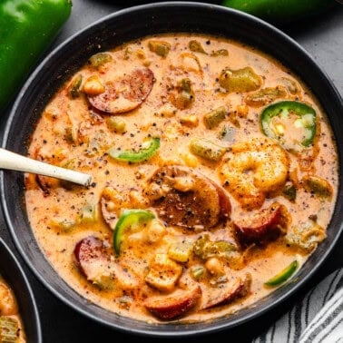 An overhead view of a black bowl of Cajun white chicken chili with a spoon sticking out.