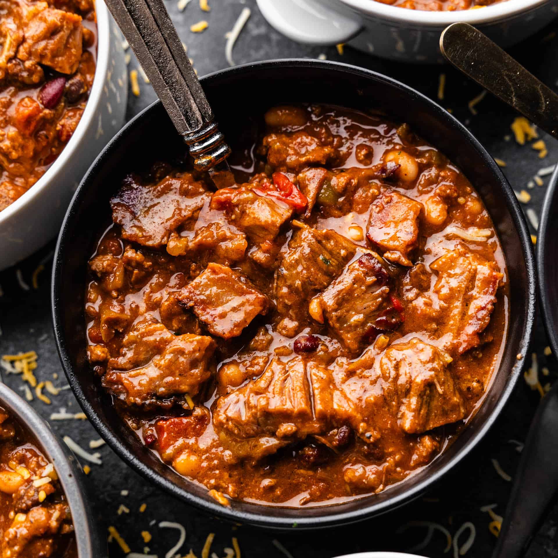 A closeup overhead view into a bowl of chili with a spoon set into it.