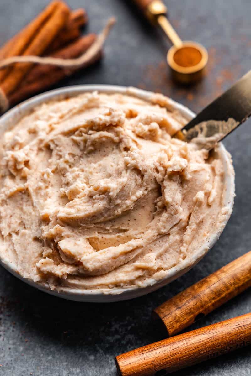 A bowl of cinnamon cream cheese butter with a knife scooping some out.