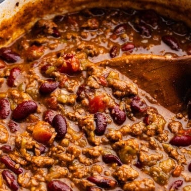 An overtop view into a pot of chili with a wooden spoon dipped in for serving.