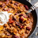 An overhead shot of a bowl of no fuss chili topped with shredded cheese and sour cream, with a spoon set into the bowl.