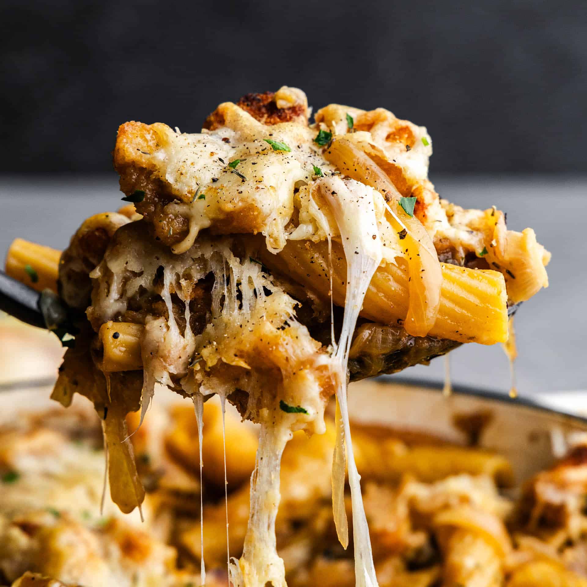 A close up view of a helping of french onion pasta casserole being scooped out of the pan.