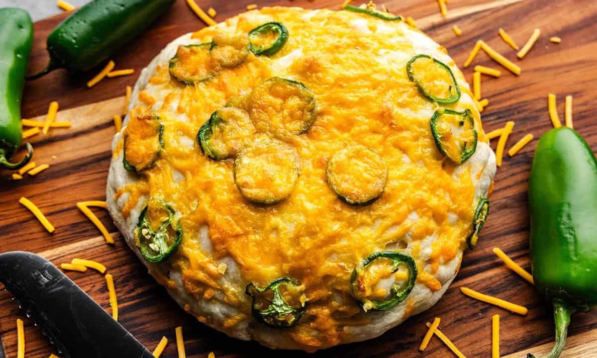 A top view of an uncut round loaf of jalapeno cheese bread set on a wooden cutting board.