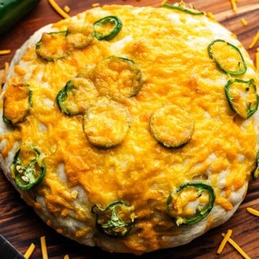 A top view of an uncut round loaf of jalapeno cheese bread set on a wooden cutting board.