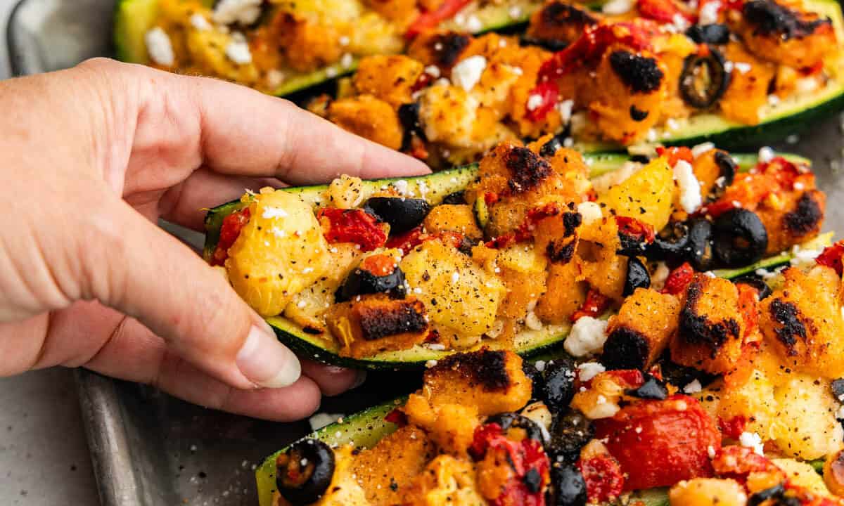 A hand lifting a stuffed zucchini boat from the pan.