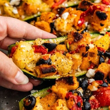 A hand lifting a stuffed zucchini boat from the pan.