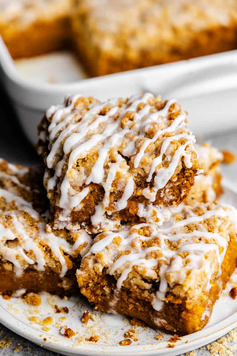 A stack of slices of pumpkin crumb cake sitting in front of the rest of the pan of cake.