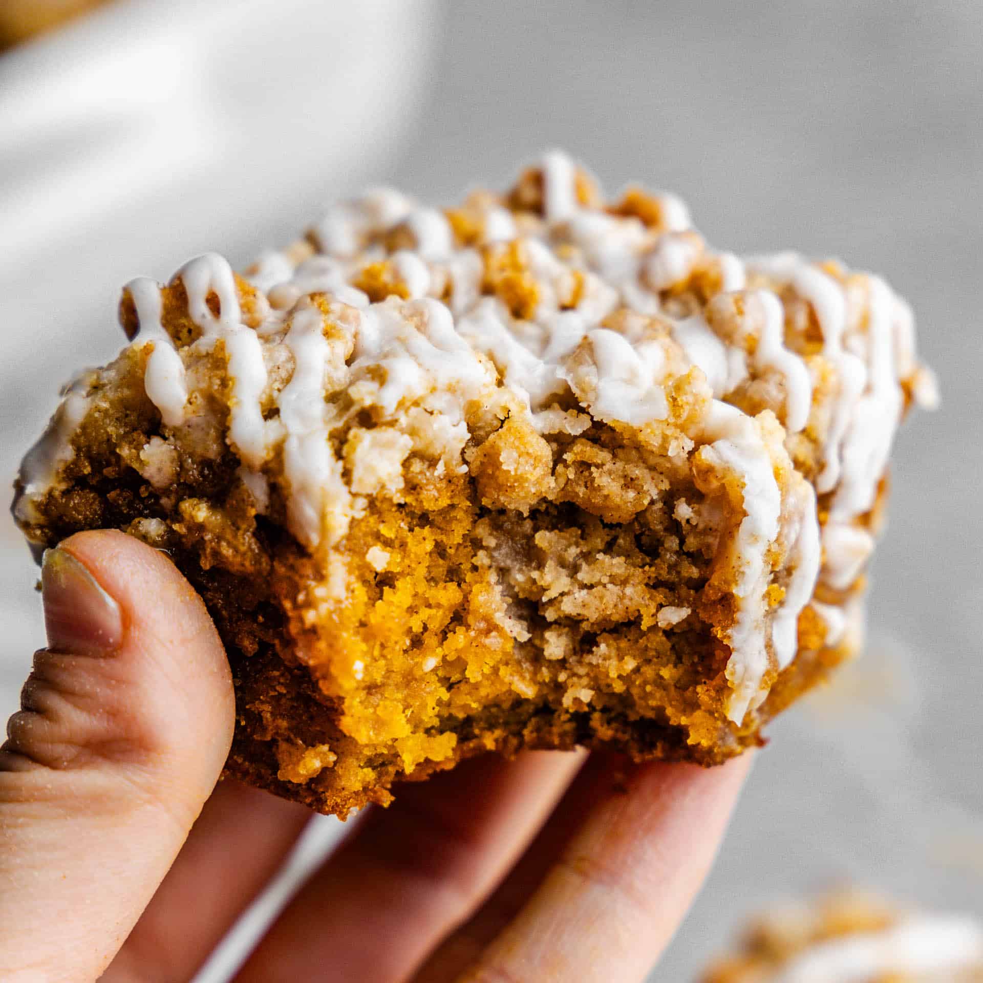 A hand holding up a slices of pumpkin crumb cake that has had a bite taken out of it.