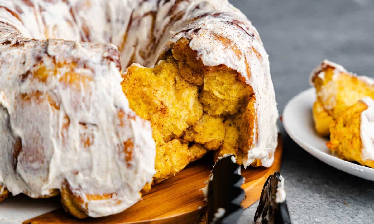 A close up of pumpkin pull apart monkey bread, frosted with a few chunks taken out to eat.