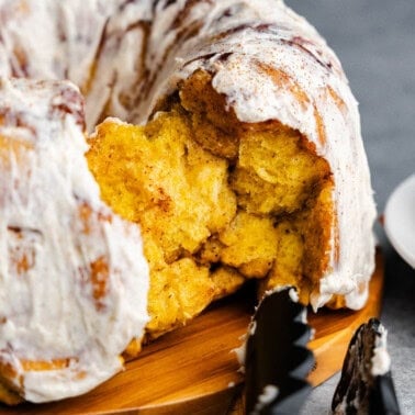 A close up of pumpkin pull apart monkey bread, frosted with a few chunks taken out to eat.