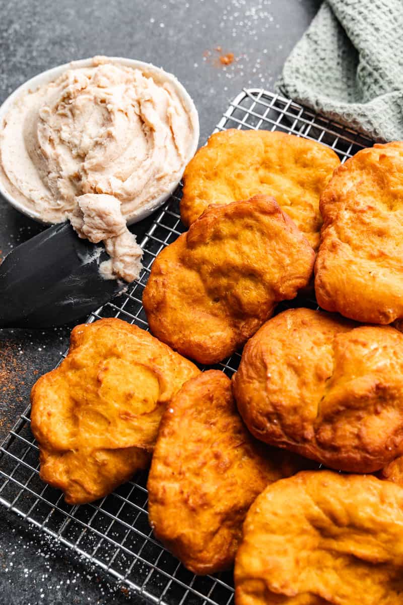 An overhead view of pumpkin fry bread on a wire rack with a bowl of cinnamon cream cheese frosting on the side.