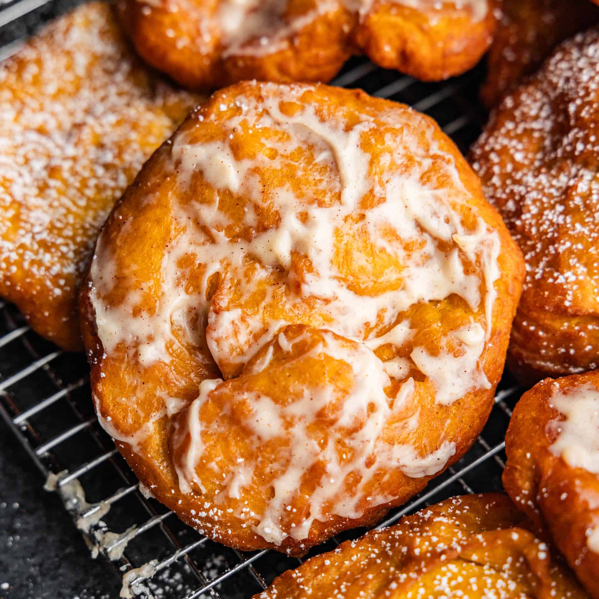 A close up view of a pile of pumpkin fry bread with cinnamon cream cheese frosting.