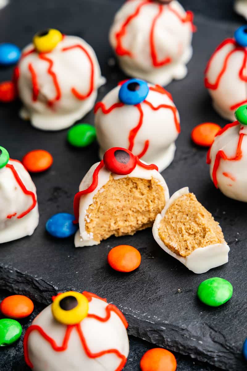 A close up of a pumpkin truffle eyeball cut open to show the pumpkin filling inside, surrounded by mini M&M's.