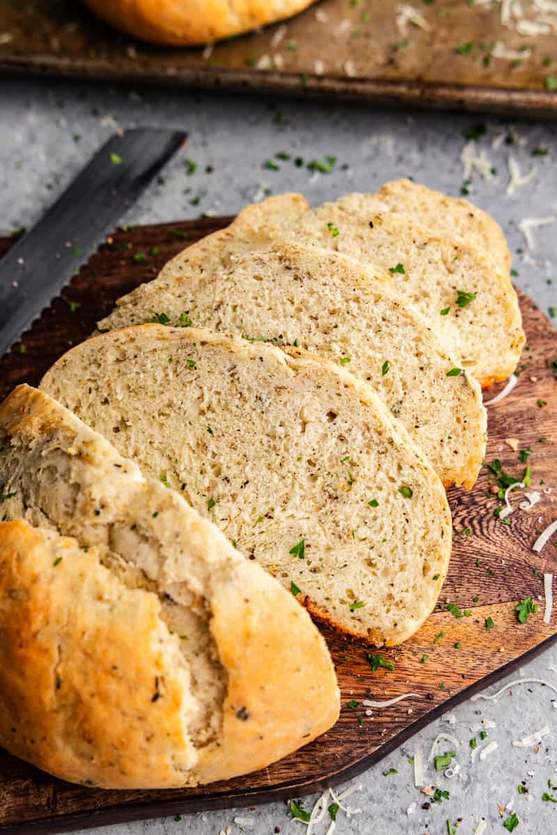 An overhead view of a loaf of garlic and parmesan herb bread that has been sliced ​​on a cutting board.