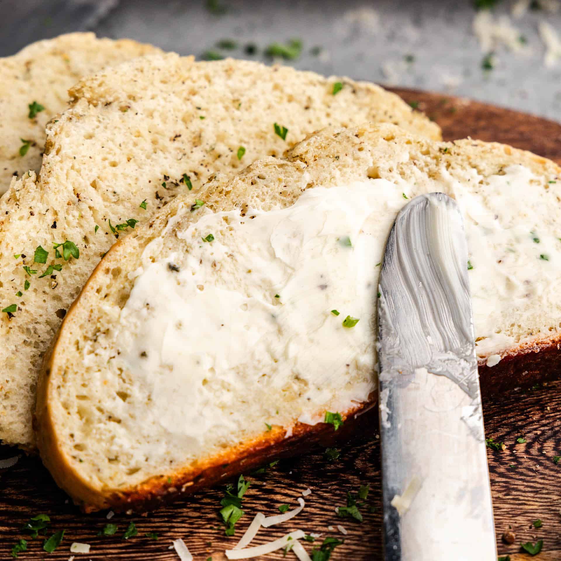 Slices of garlic parmesan herb bread with the top slice having butter spread on top.