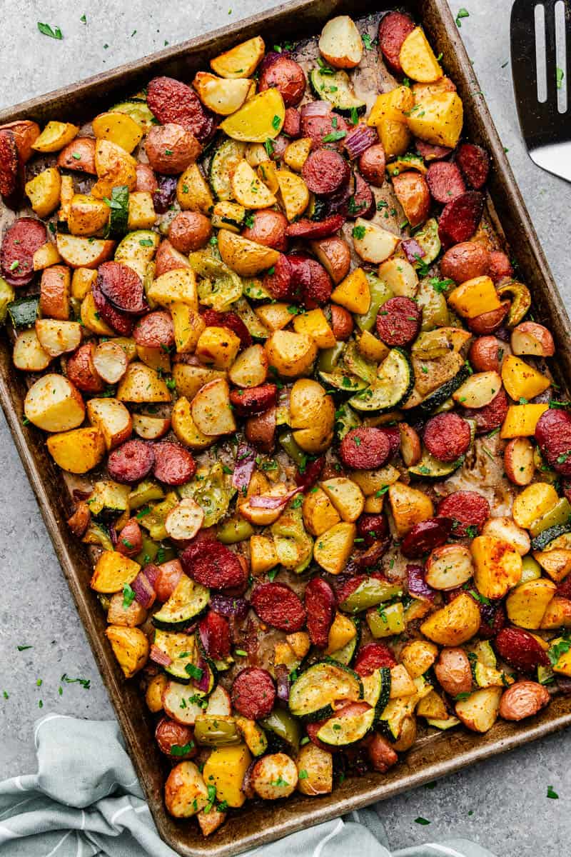 An overhead view of a sheet pan filled with browned cut potatoes, sausage slices and peppers.