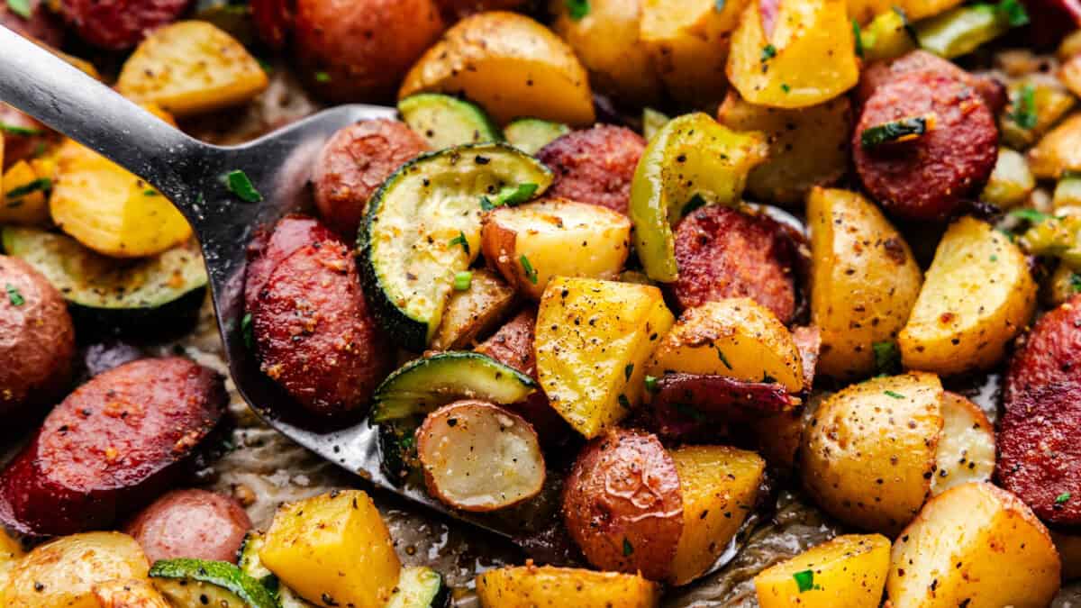 A close up view of a spatula lifting diced potatoes, peppers and sausage coins.