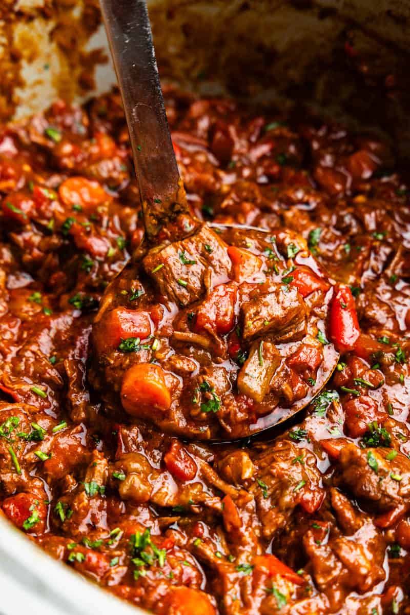 A ladle scooping a helping of Texas-style beef chili from the crock of a slow cooker.