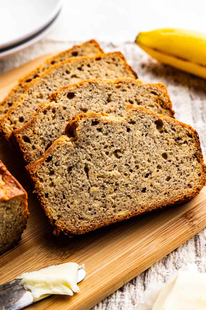 Slices of banana bread placed against each other like falling dominoes on a cutting board.