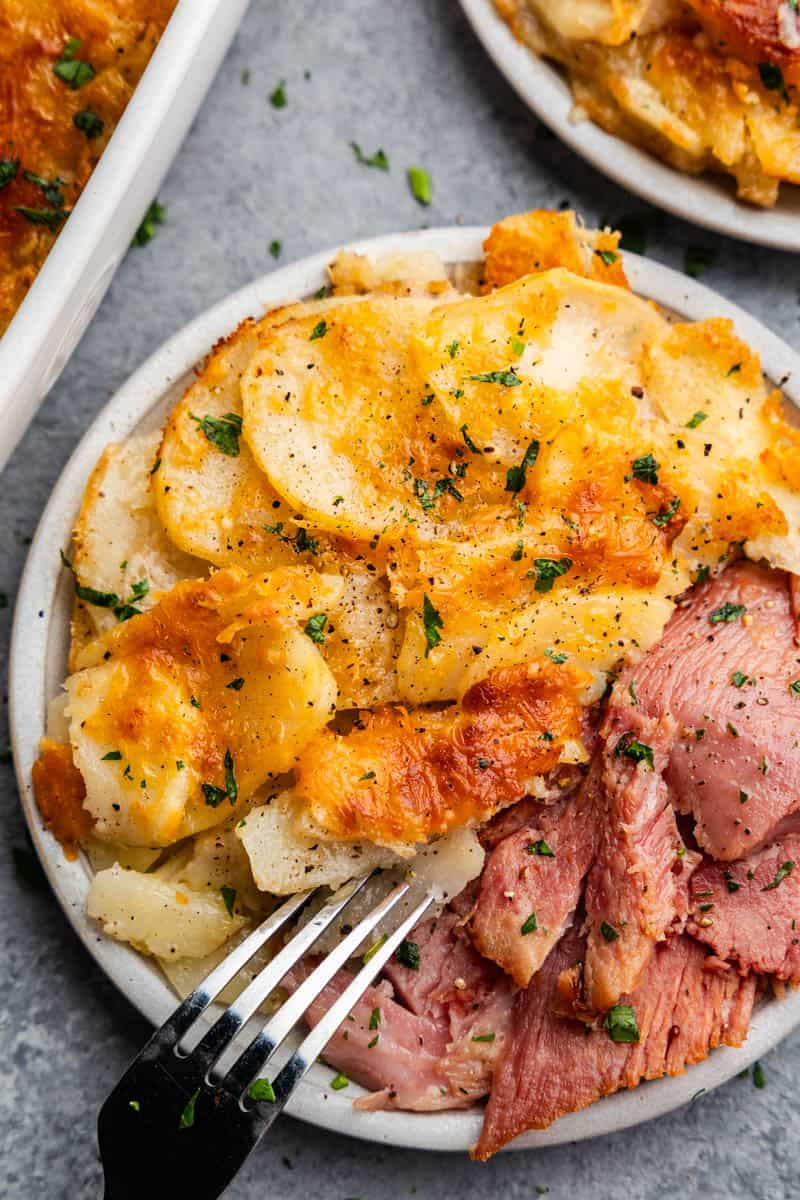 A plate filled with a serving of cheesy scalloped potatoes set next to ham.