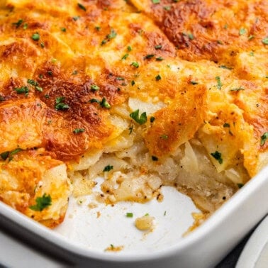 An angled view of a casserole dish filled with cheesy scalloped potatoes, with a corner piece missing.