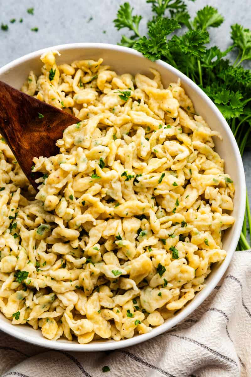 Overhead view of granny setting a serving bowl filled with German spaetzle and a wooden spoon between the food.